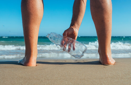 Man standing at seashore picking up empty plastic bottle, close-up