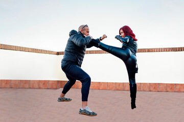 Redheaded woman wearing black leather catsuit fighting against man on rooftop