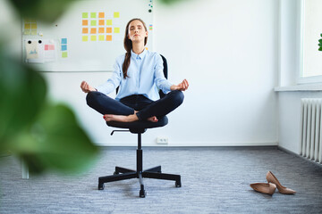 Serene young woman meditating while sitting on office chair
