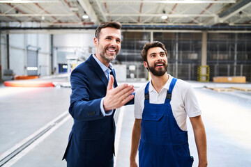 Happy businessman and worker in a factory