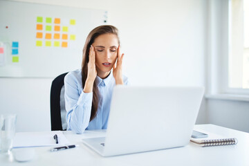 Young businesswoman sitting in office suffering from headache