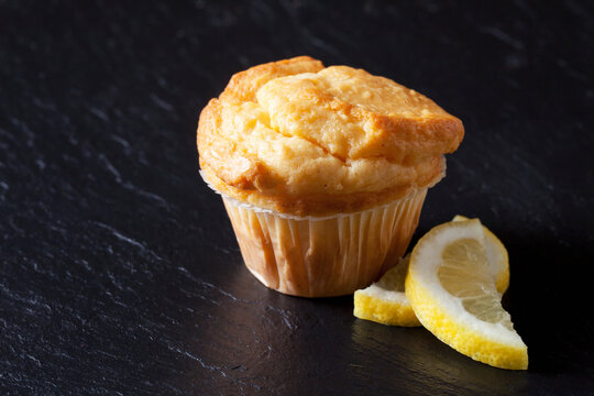 Fresh lemon muffin on black slate with lemon slices