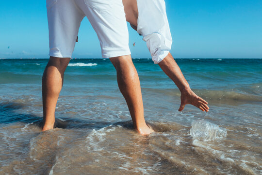 Man standing at seashore picking up empty plastic bottle
