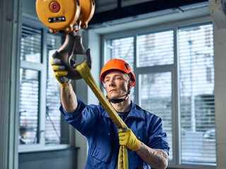 Industrial worker fixing hoist sling on indoor crane