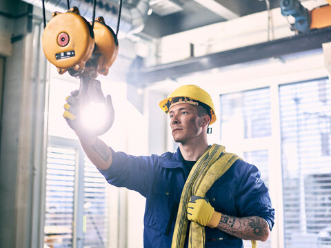 Industrial worker fixing hoist sling on indoor crane