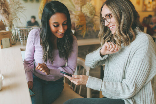Two women using smartphone in a cafe - Powered by Adobe