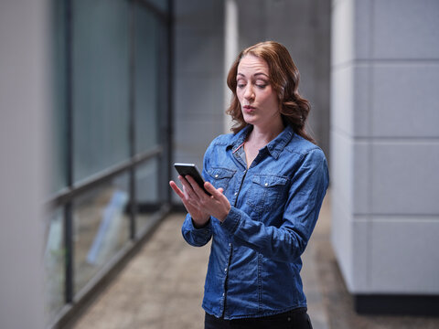 Surprised businesswoman using cell phone on modern office floor