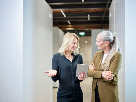 Two businesswomen sharing tablet on office floor