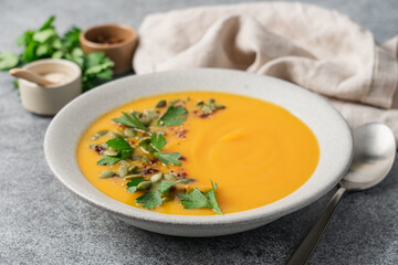 Pumpkin puree cream soup with seeds, spices and green parsley leaves in gray terracotta plate on white plate. Autumn traditional food