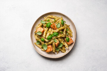 Penne pasta with baked salmon, pesto and fresh basil in a plate, top view, white background