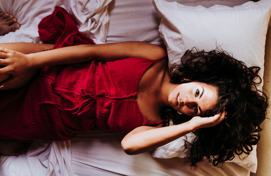 Portrait of young woman wearing red dress lying on bed, top view