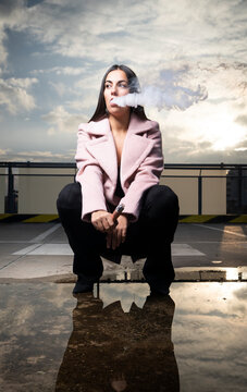 Portrait of fashionable young woman smoking electronic cigarette on parking level