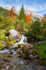 kleiner gebirgsbach im herbst am fuß des hochkönig unter blauem himmel, little creek in indian summer austrian alps salzburg looks like canada alaska