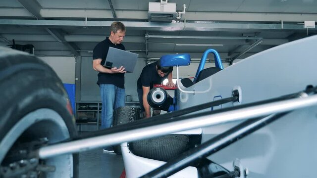 Mechanics are talking about a racing car in the garage