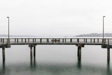 Fototapeta na wymiar Wooden Pier with Bench over Calm Water on Foggy Day (Commencement Bay, Tacoma, WA)