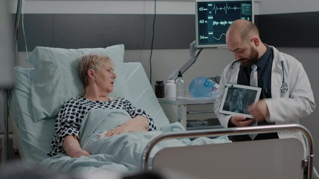 Medic explaining radiography diagnosis on tablet to patient with disease. Doctor showing x ray scan on device for healthcare of retired woman with IV drip bag and nasal oxygen tube.