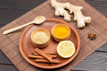Dry ginger and turmeric powder in wooden bowls, lemon wedge on ceramic plate.