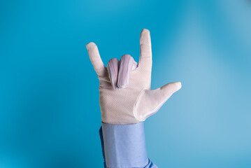 Fototapeta premium A man's hand in a white fabric anti-static anti-slip glove shows the rock symbol on a blue background.