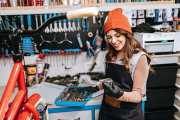 Beautiful young female mechanic enjoying while repairing bicycles in a workshop..