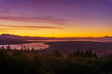 Golden sunrise over valley with alpine mountains in silhouette on horizon and high-rises peaking...