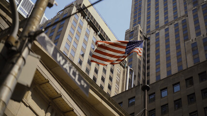 Wall Street sign with American flags in the background, shot in the heart of the business world in Manhattan. Business, finance, worldwide stock trade and economics concept.