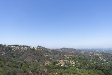 View of Hollywood Hills seen from Mulholland Drive on a sunny summer day. Houses and trees