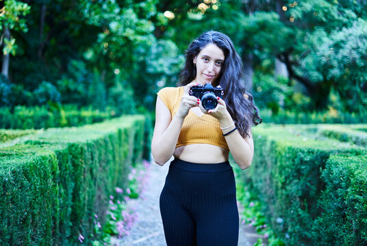 brunette girl taking pictures in the park with analog camera
