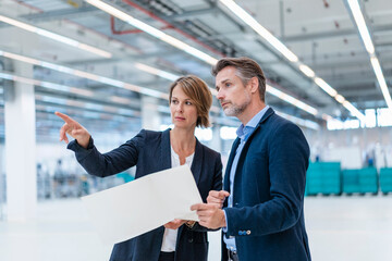 Businessman and businesswoman discussing plan in a factory hall