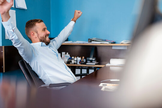 Happy businessman cheering at desk in office