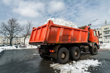 Tractor loader machine uploading dirty snow into dump truck. Cleaning city street, removing snow and ice after heavy snowfalls and blizzard. Snowplow outdoors clean pavement sidewalk road driveway