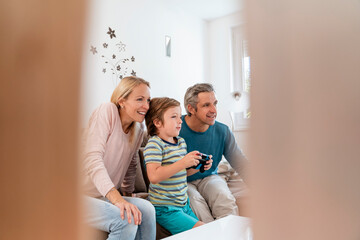 Happy parents with son playing video game on couch at home