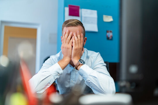 Businessman sitting at desk in office with hands covering face
