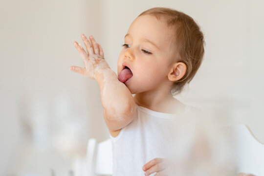 Little girl licking her arm while making a cake in kitchen at home