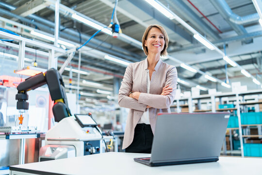 Smiling businesswoman with laptop in a modern factory hall