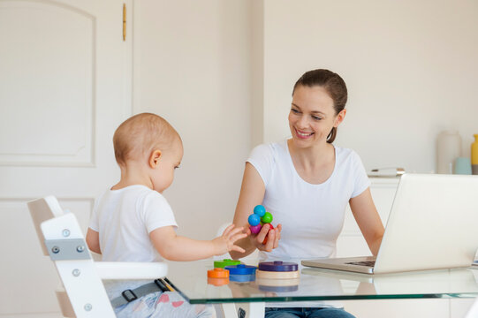 Smiling mother using laptop playing with little daughter at table at home