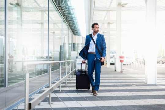 Businessman with trolley and smartphone at airport
