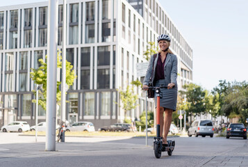 Happy businesswoman riding electric scooter on the street