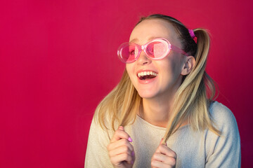 A beautiful happy girl with two tails laughs cheerfully in front of her pink glasses. Retro style concept