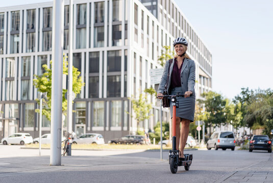Happy businesswoman riding electric scooter on the street