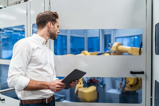 Businessman with tablet looking at robot in a modern factory