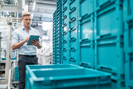 Businessman using tablet in a factory hall with boxes