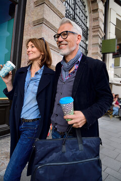 Smiling mature couple with reusable bamboo cups walking in the city