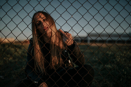 Portrait of young woman sitting behind wire mesh fence giving the finger