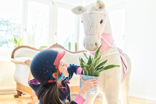 Girl feeding her toy horse with house plant at home