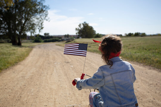 Girl with American flag riding bicycle on path in remote landscape
