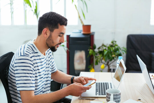 Young man using laptop and cell phone at desk in office
