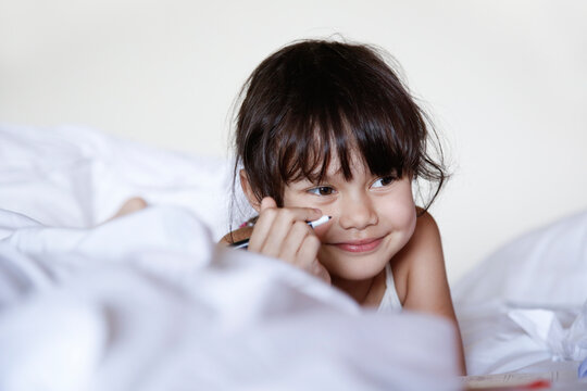 Portrait of smiling little girl lying in bed with felt tip pen