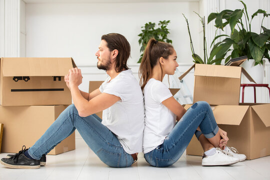Couple with cardboard boxes sitting on the floor in new home