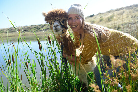 Portrait of smiling blond woman head to head with alpaca in nature