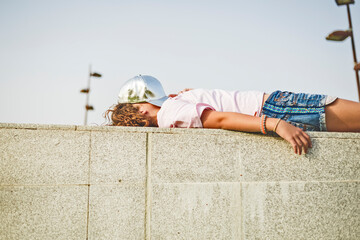 Girl lying on wall, basecap on head, obscured face